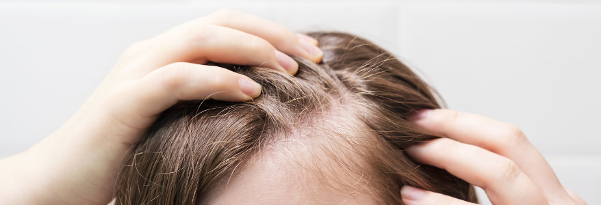 Woman touching her hair close up on white tiles background, hair loss concept.